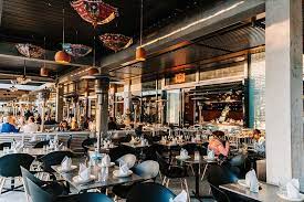 A spacious and modern restaurant interior with eclectic hanging lamps, diners seated at tables, and a bustling atmosphere.